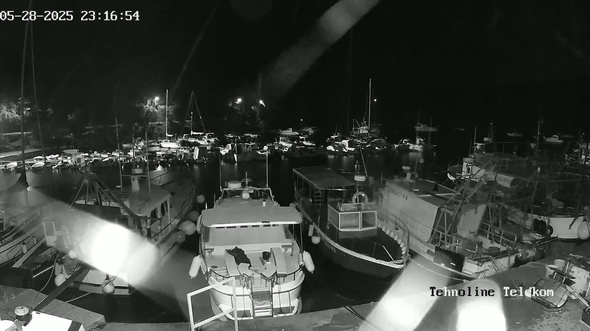 A nighttime, black and white view of numerous boats docked at a marina in calm water.