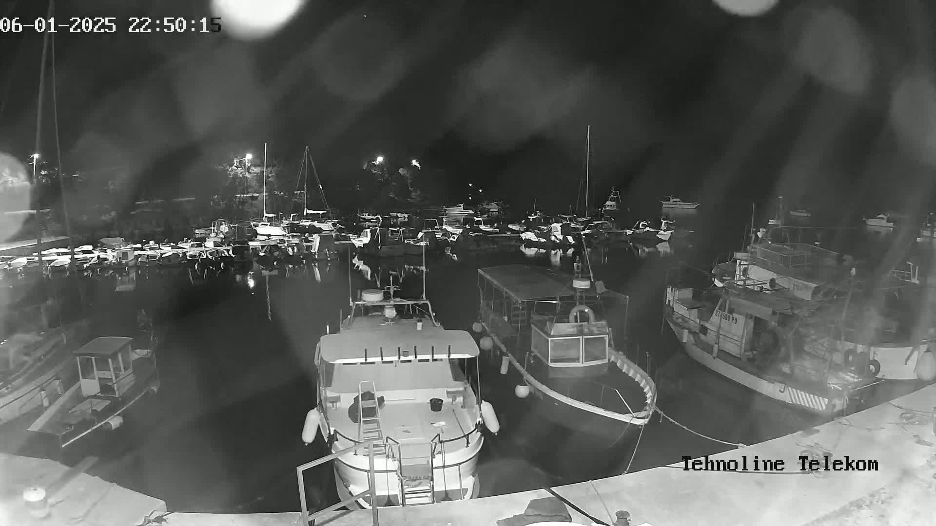 A nighttime, rain-streaked view of a marina filled with numerous boats, some of which are larger vessels.
