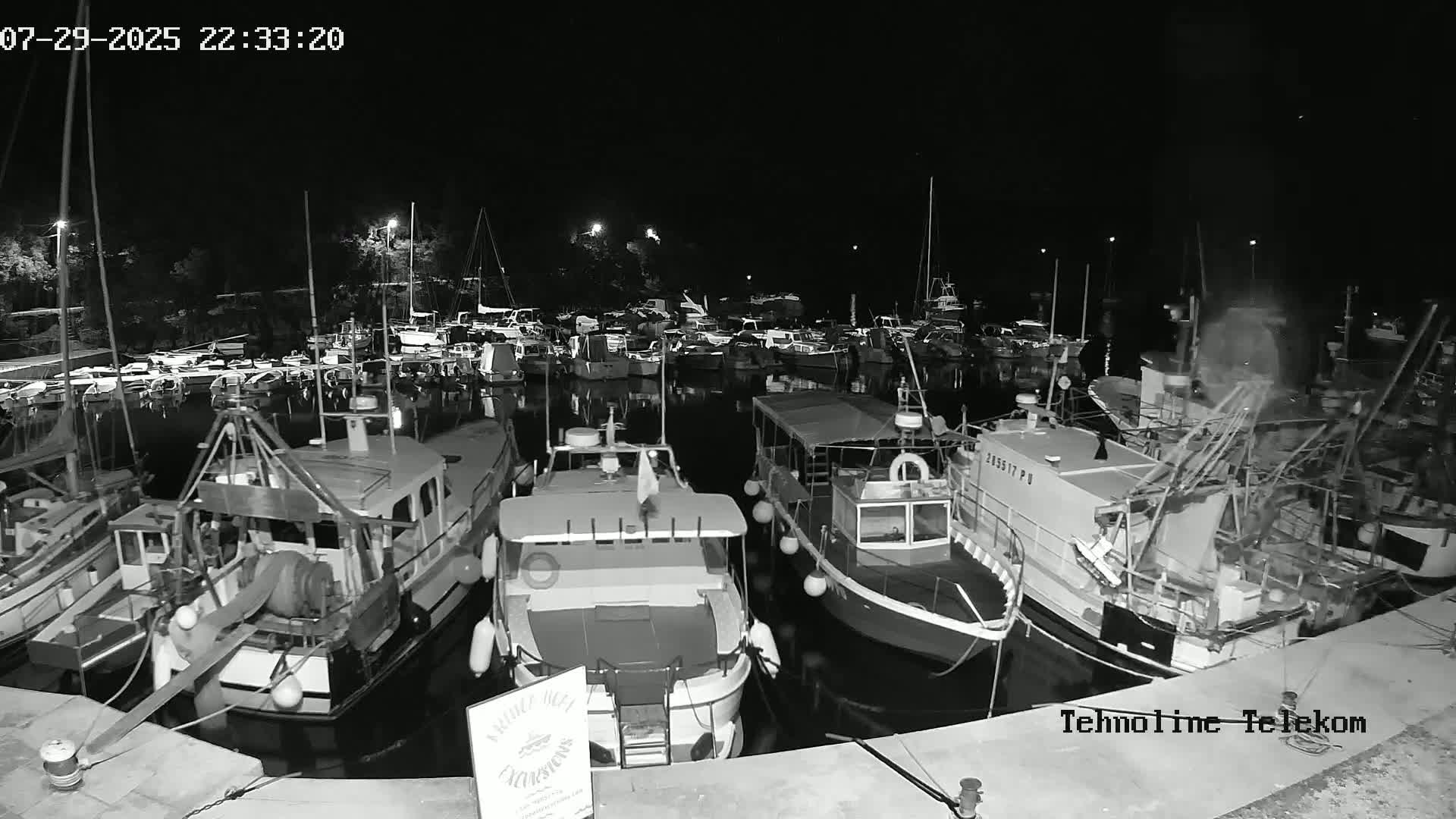 A harbor filled with numerous boats and yachts on a sunny day, nestled in a cove surrounded by lush green hills.