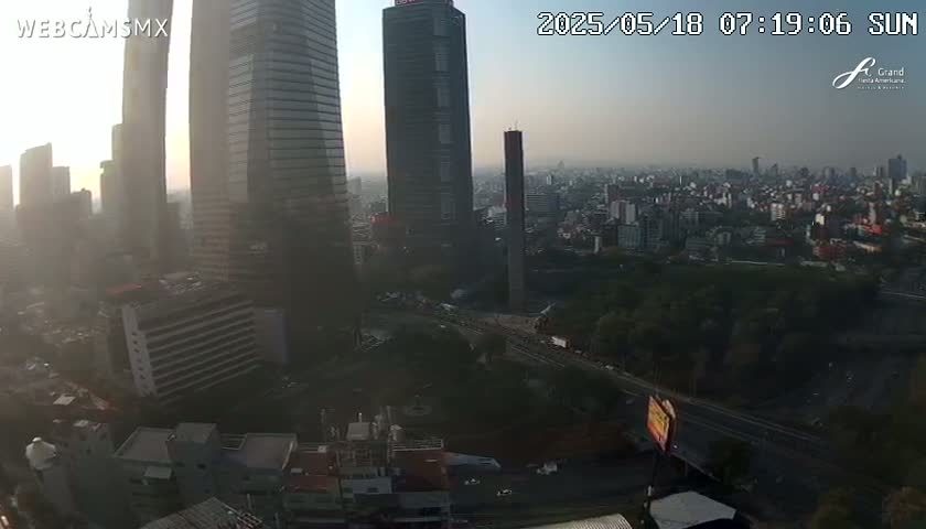 A hazy sunrise illuminates a cityscape of tall buildings and surrounding low-rise structures, with a highway visible below.