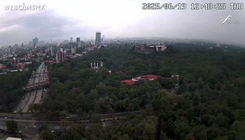 A hazy, overcast day reveals a cityscape and a large expanse of green parkland, with a highway visible below.