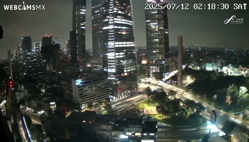 A nighttime cityscape view of tall buildings and surrounding streets, with a park visible below.