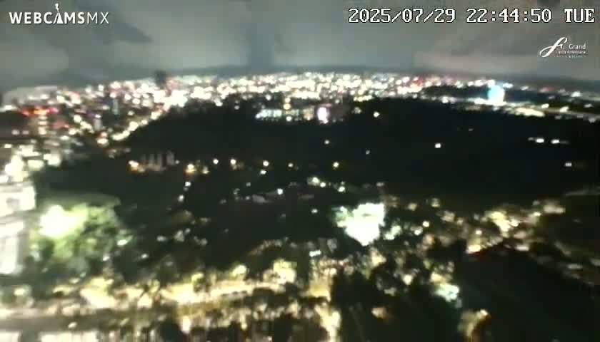 A nighttime aerial view of a city with tall buildings and illuminated roads and parks, under a mostly clear sky.