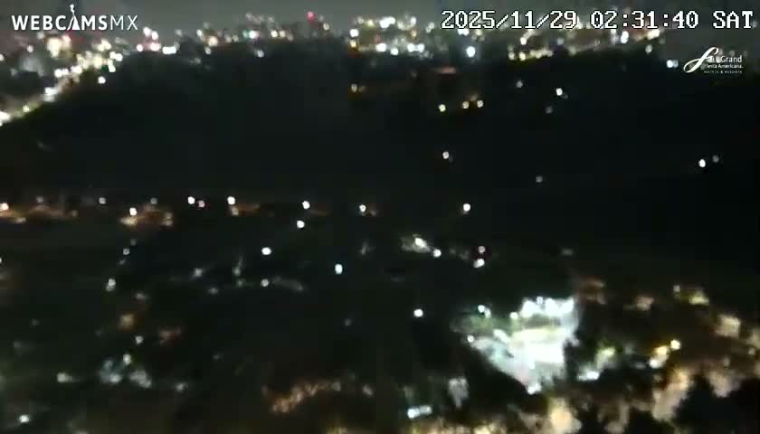 A blurry, elevated nighttime view reveals a city or town with numerous scattered lights under clear skies.