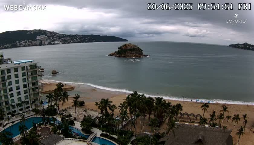 A coastal scene under a cloudy sky shows a sandy beach lined with palm trees, a resort with pools, and a small island in the calm ocean.