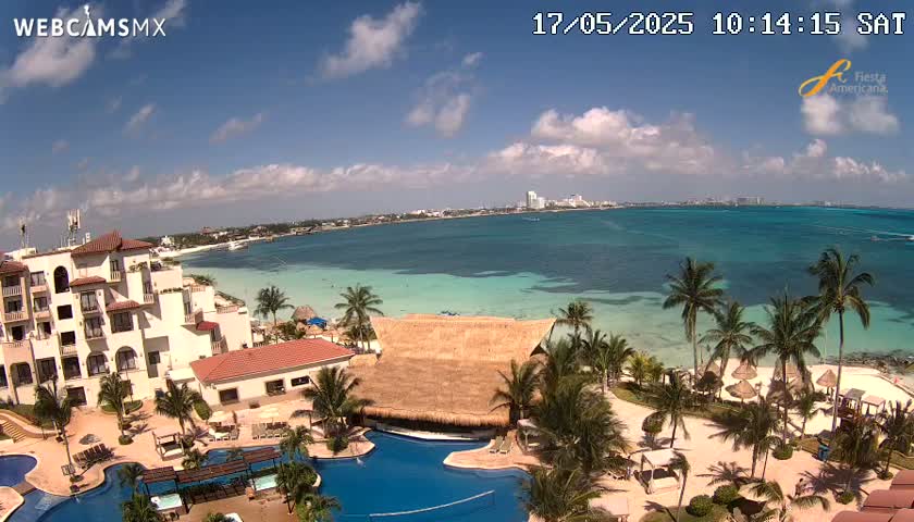 An aerial view of a resort on a beach with turquoise water under a partly cloudy sky.