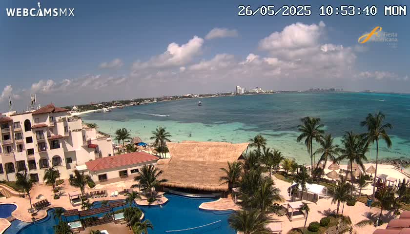 An aerial view shows a resort on a beach with turquoise water under a partly cloudy sky.