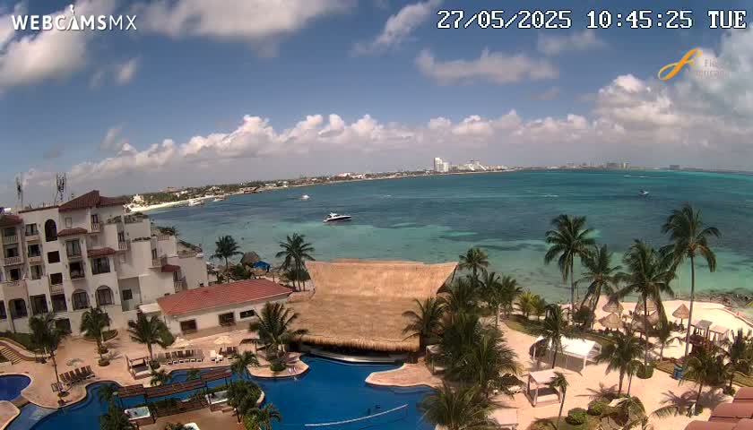 A resort with multiple pools overlooks a calm, turquoise ocean under a partly cloudy sky.