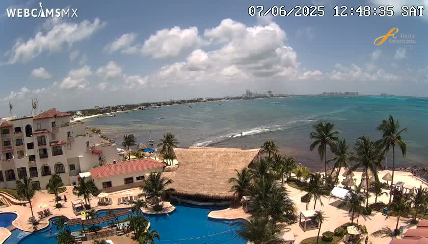 A resort with multiple pools and palm trees overlooks a calm, partly cloudy ocean.