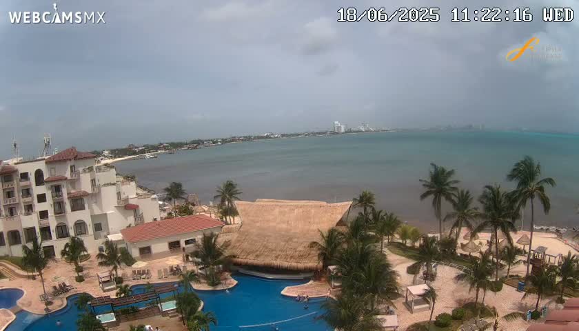 A resort with swimming pools overlooks a calm ocean under a partly cloudy sky.