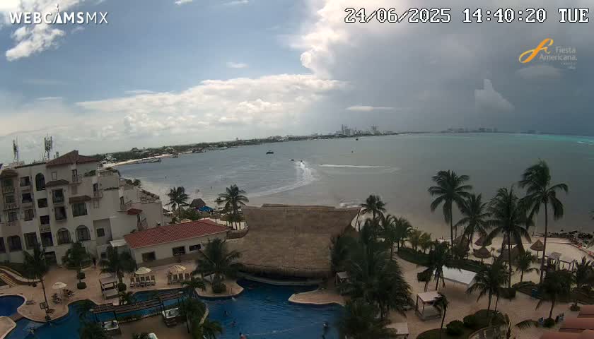 An elevated view shows a resort with pools and palm trees overlooking a calm ocean under partly cloudy skies, with darker clouds gathering on the horizon.
