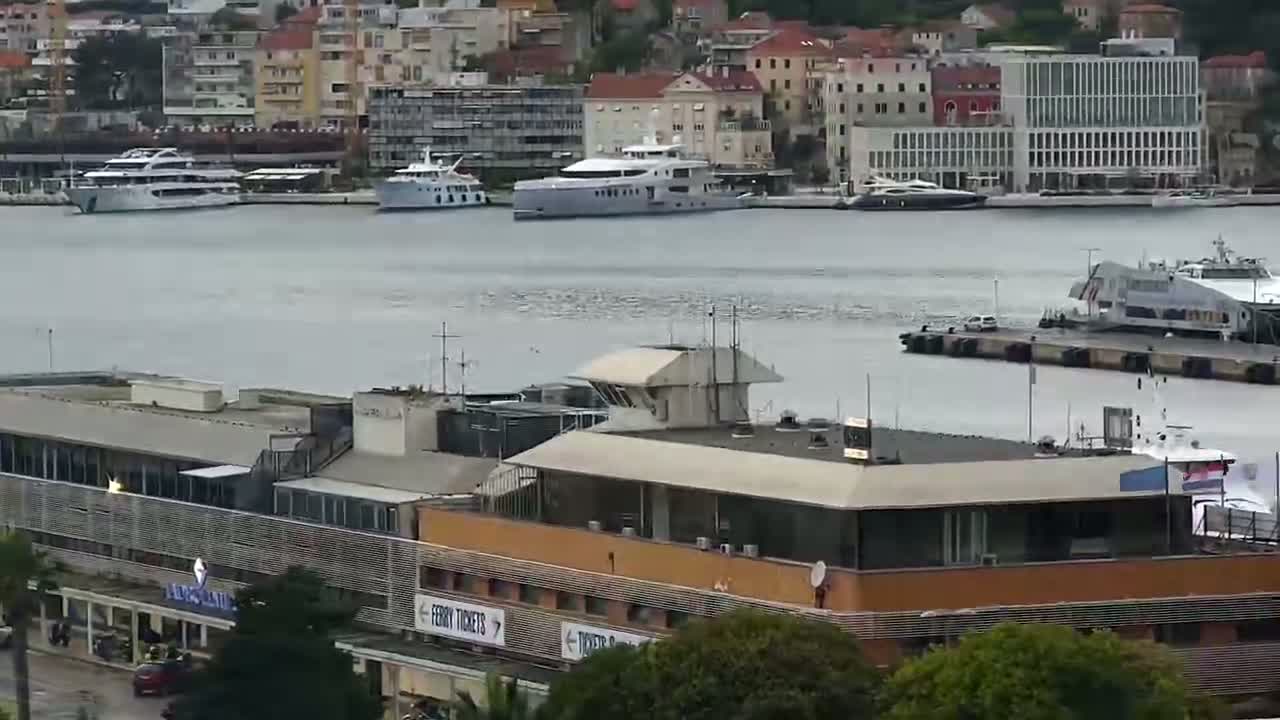 A harbor with several boats, including yachts and ferries, is seen from an elevated vantage point on an overcast day.