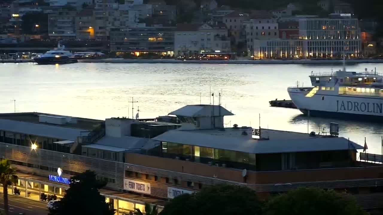 A ferry is docked near a building at a harbor at twilight, with calm water reflecting the light.