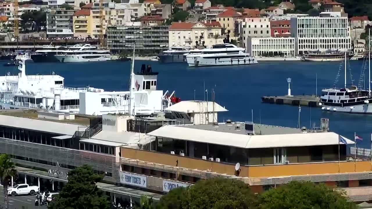 A ferry terminal building is situated beside a harbor filled with various boats and yachts, on a sunny day.