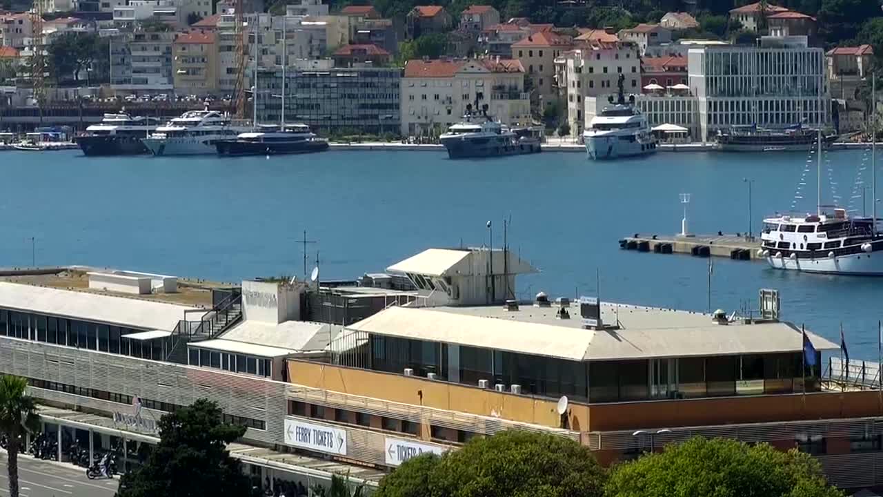 A harbor filled with yachts and ferries on a sunny day, overlooked by a multi-story building.