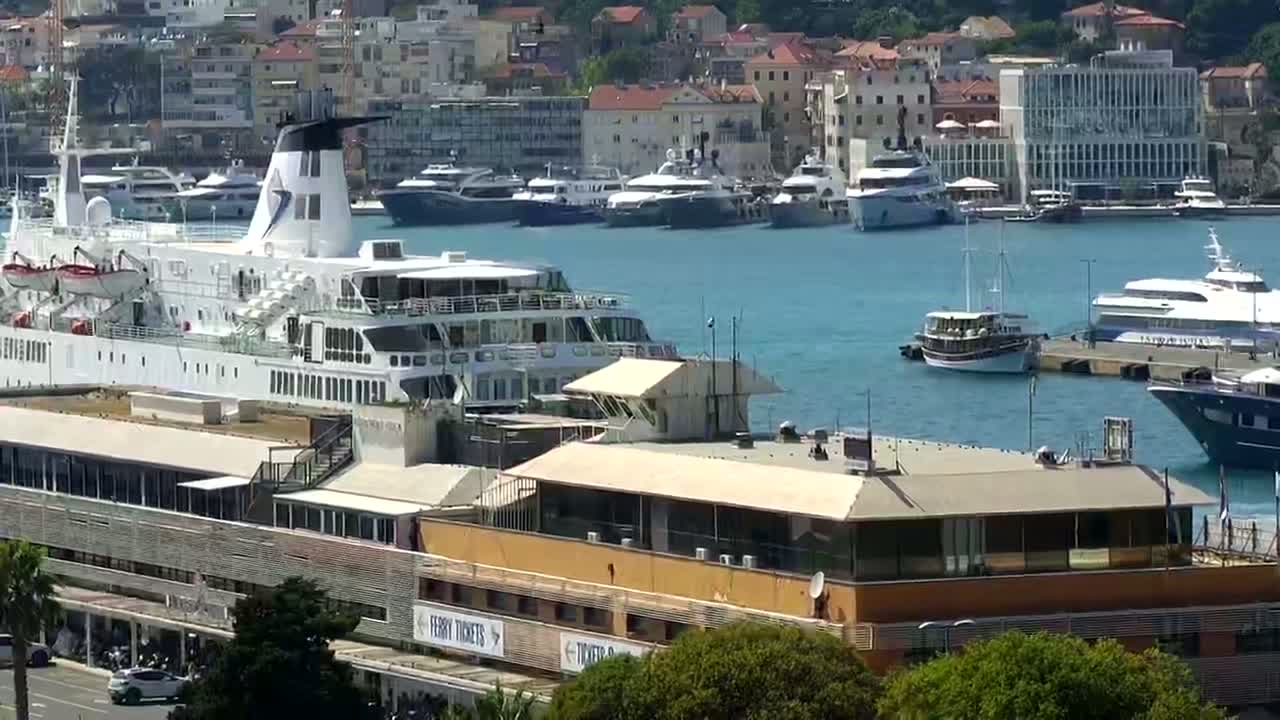 A large ferry is docked at a harbor filled with various boats and yachts on a sunny day.