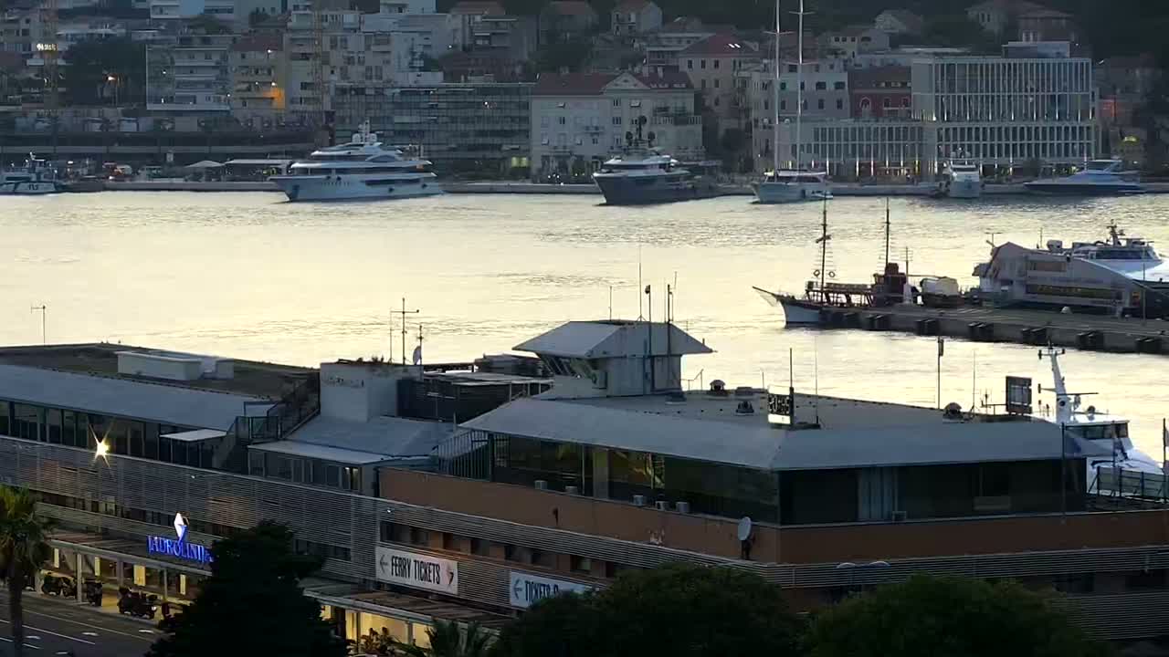 A harbor at sunset with several boats docked, including yachts and ferries, near a large building.