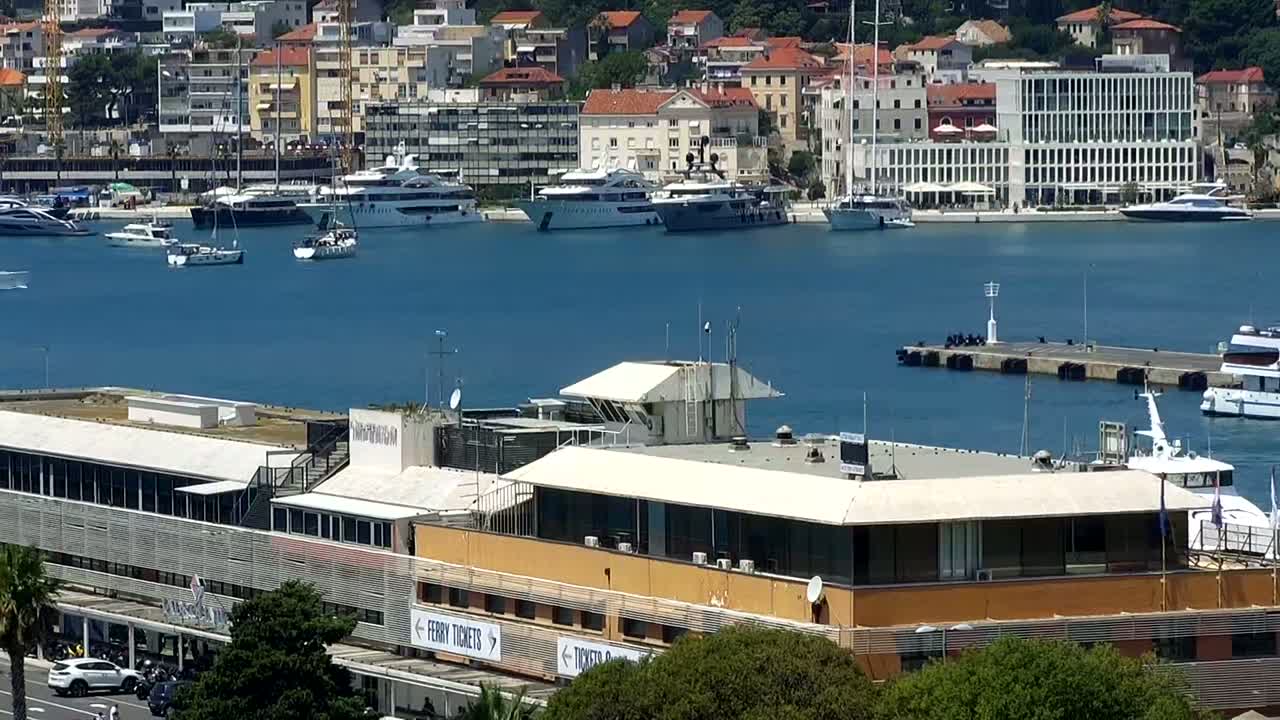 A harbor filled with yachts and boats on a sunny day, with a large building at the forefront.