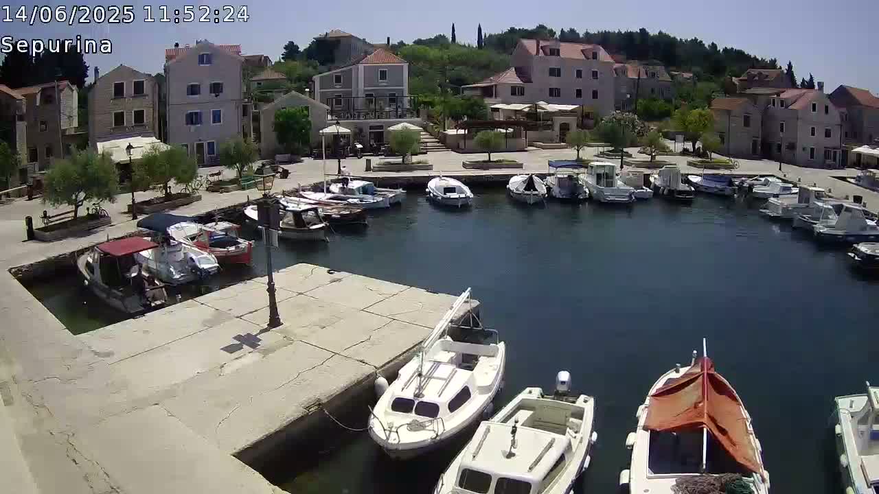 A sunny harbor filled with numerous boats is nestled beside a village of stone buildings on a clear day.