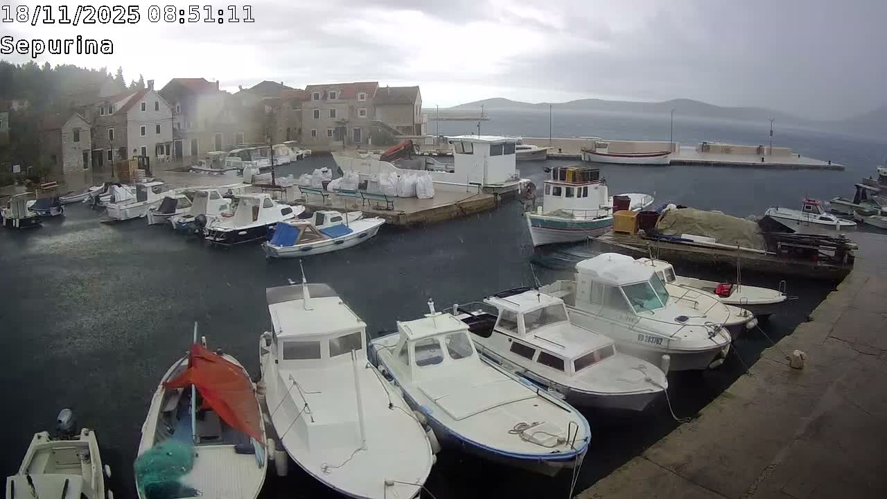 A sunny harbor filled with numerous boats is nestled beside a village of stone buildings on a clear day.