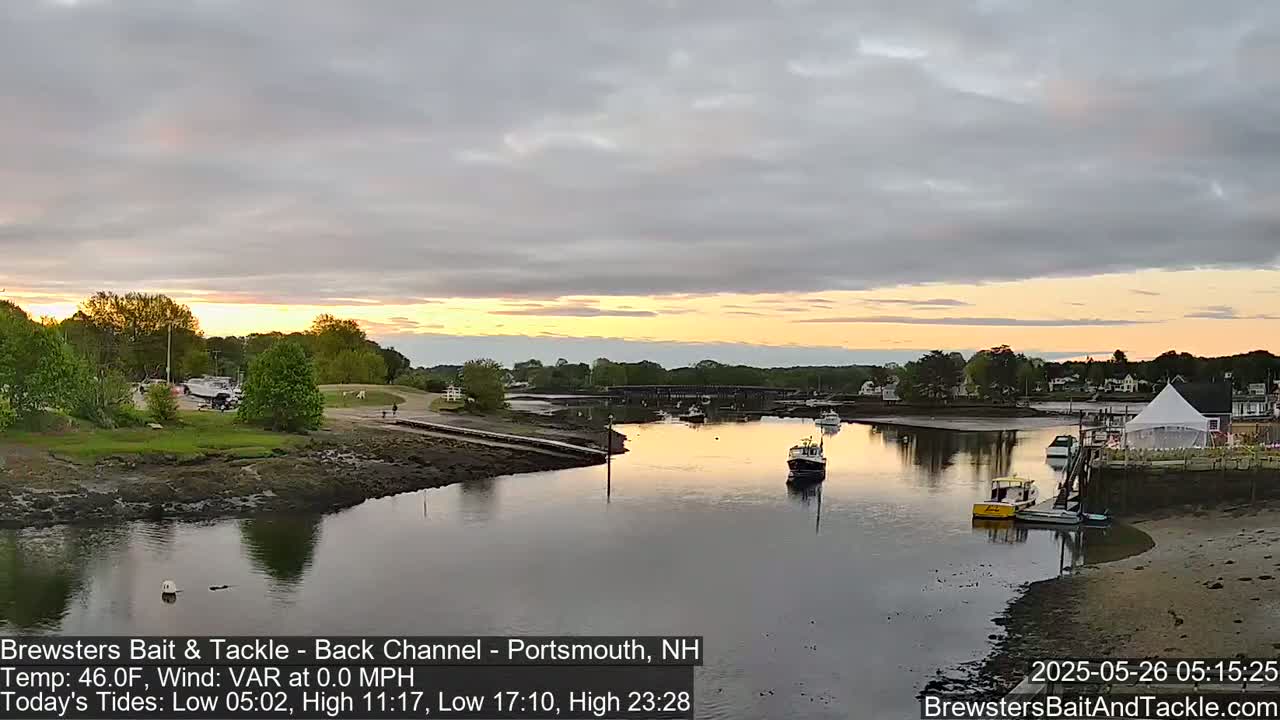 A calm river at sunset, with several small boats moored near a shoreline and a white tent visible in the distance.