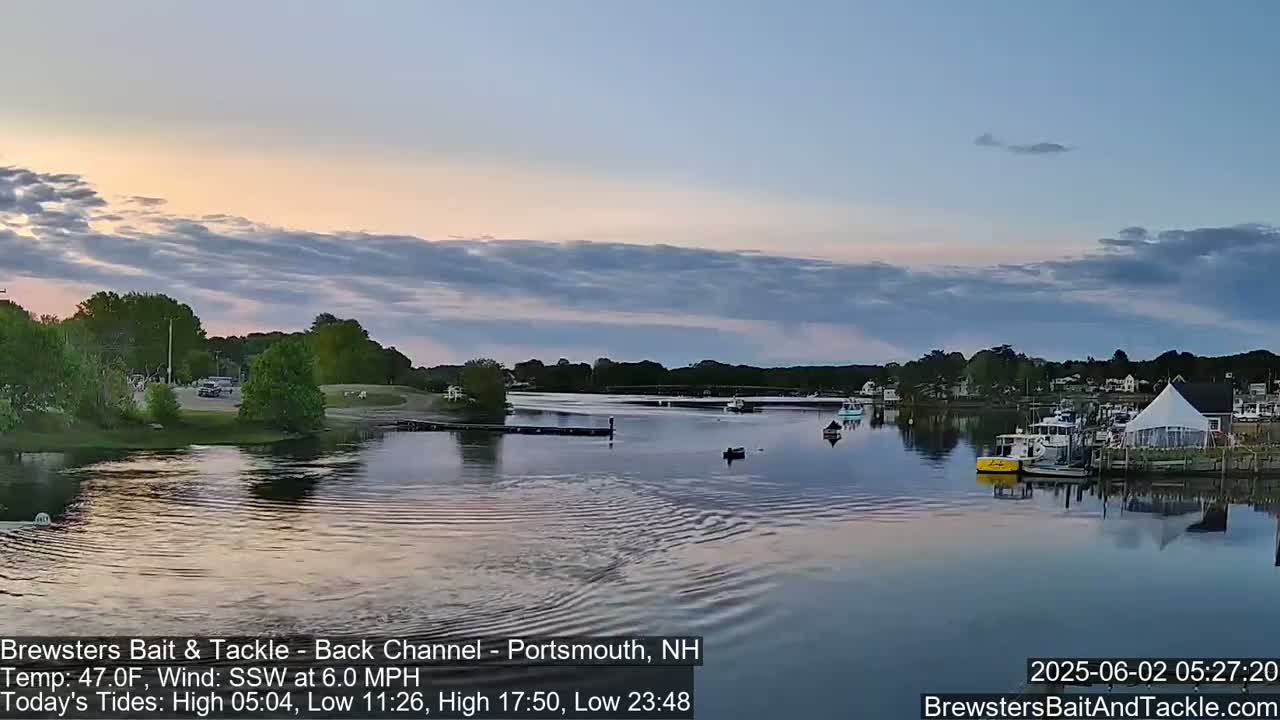 A calm body of water with several boats is seen at sunset under a partly cloudy sky.