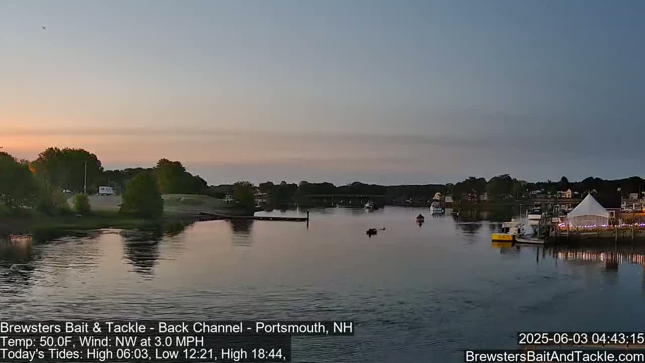 A calm river at sunset, with a few boats and a large white tent visible on the shore.