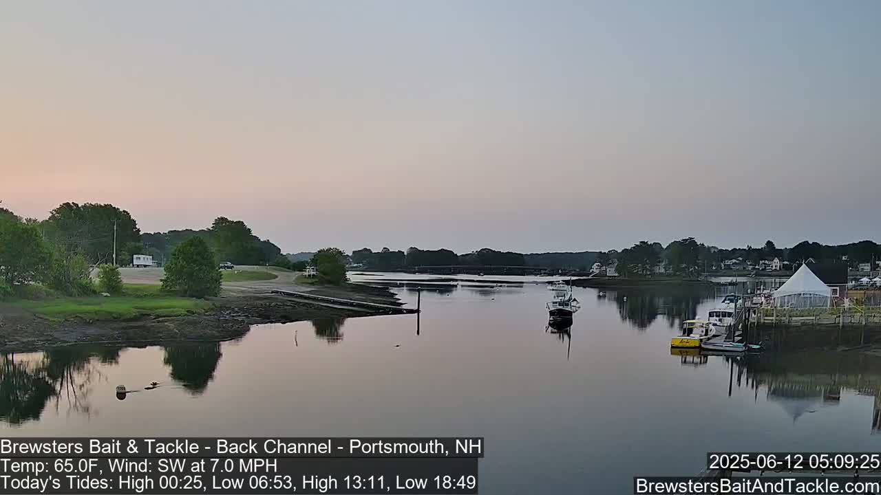 A calm river at sunset, with several boats moored near a shoreline featuring trees and buildings.