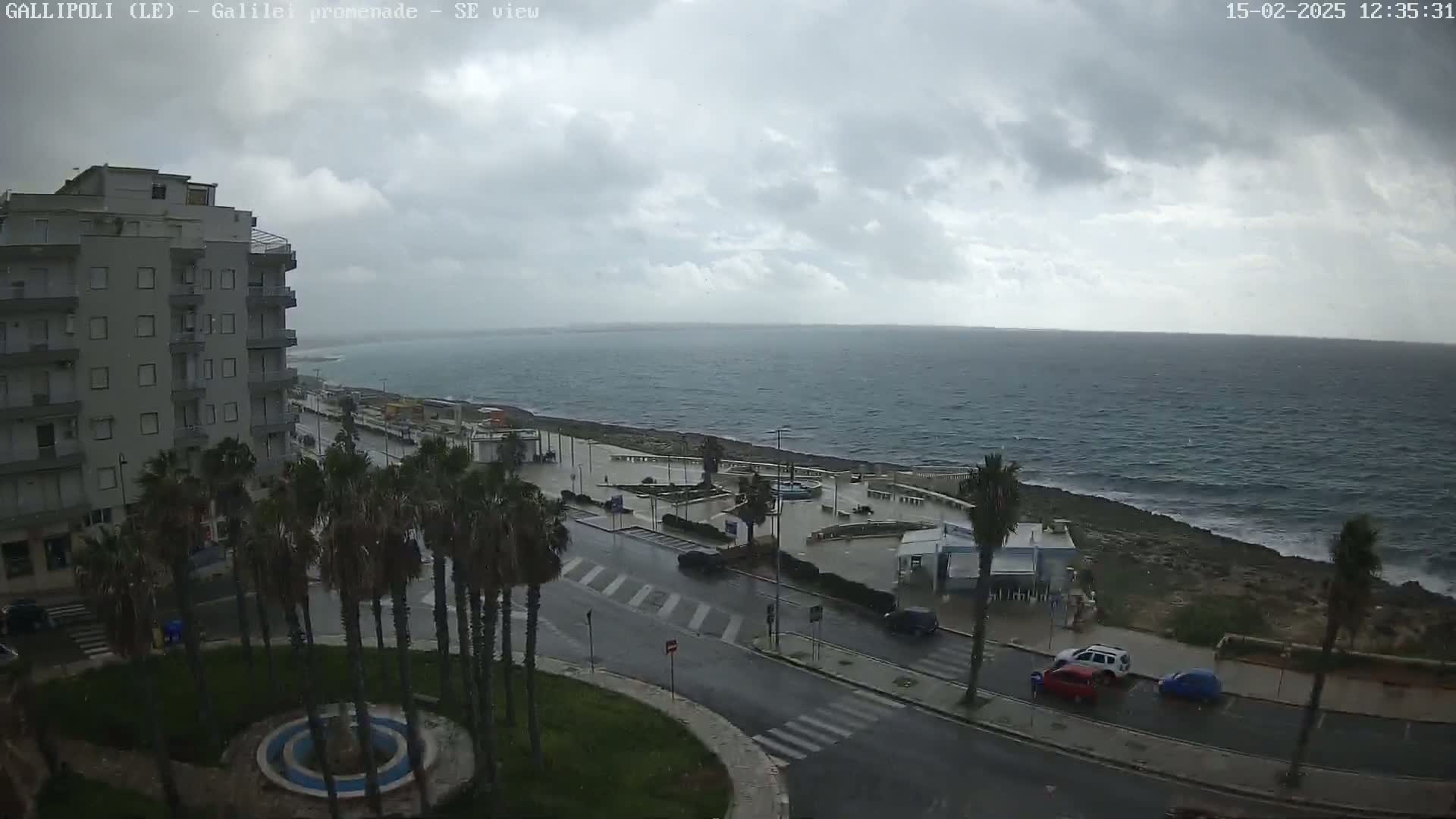 A seaside town is seen on an overcast day with rain on the streets and a choppy sea.