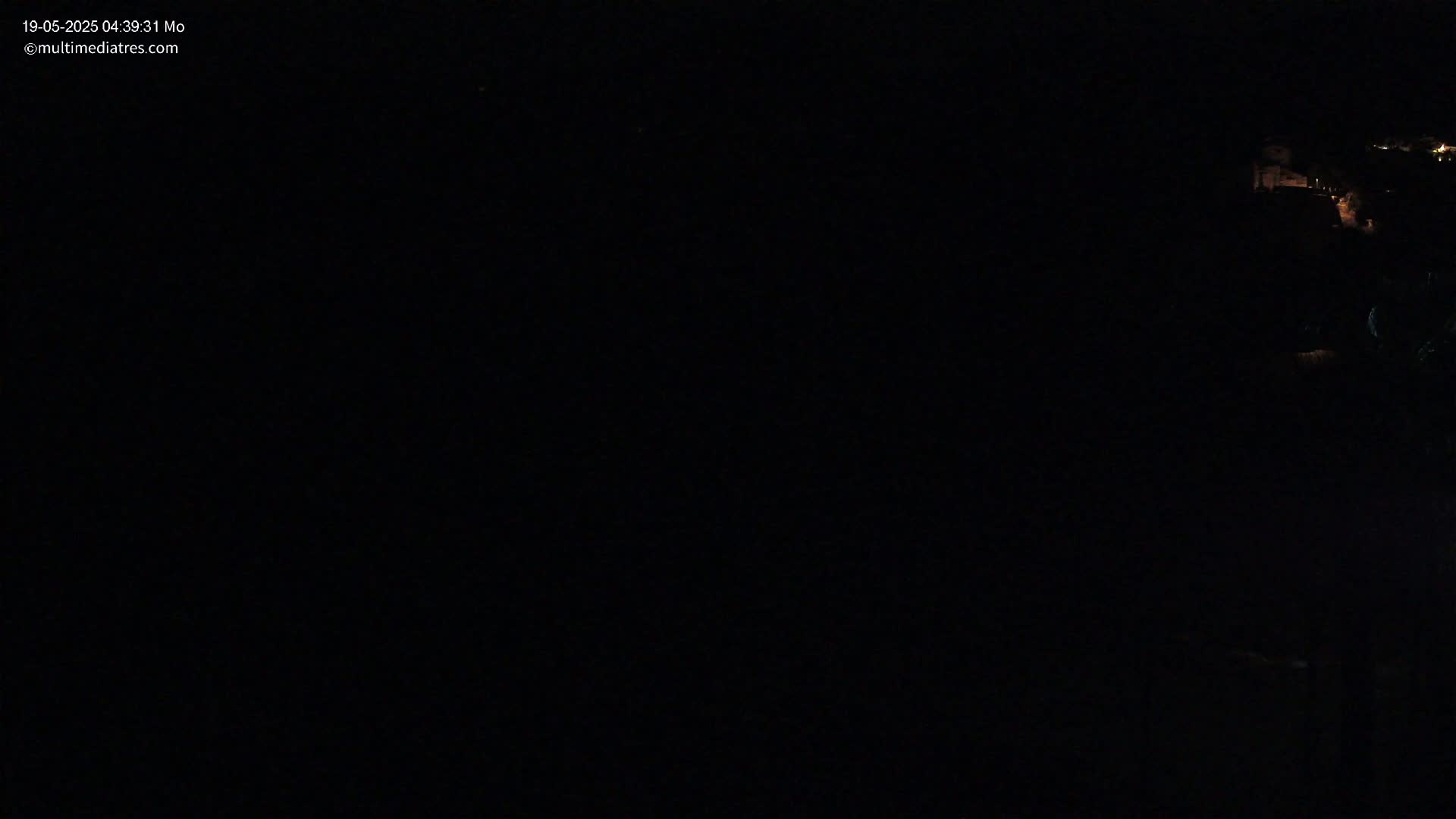 A mostly dark nighttime scene shows faintly lit structures in the distance on a hill.