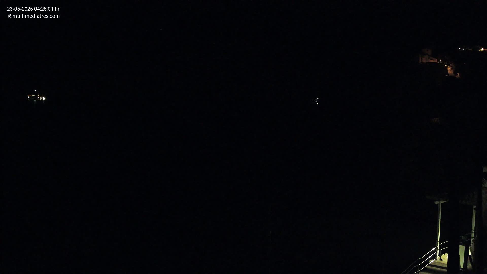 A dark nighttime scene shows a body of water with faint lights in the distance and a dimly lit structure with stairs in the lower right corner.