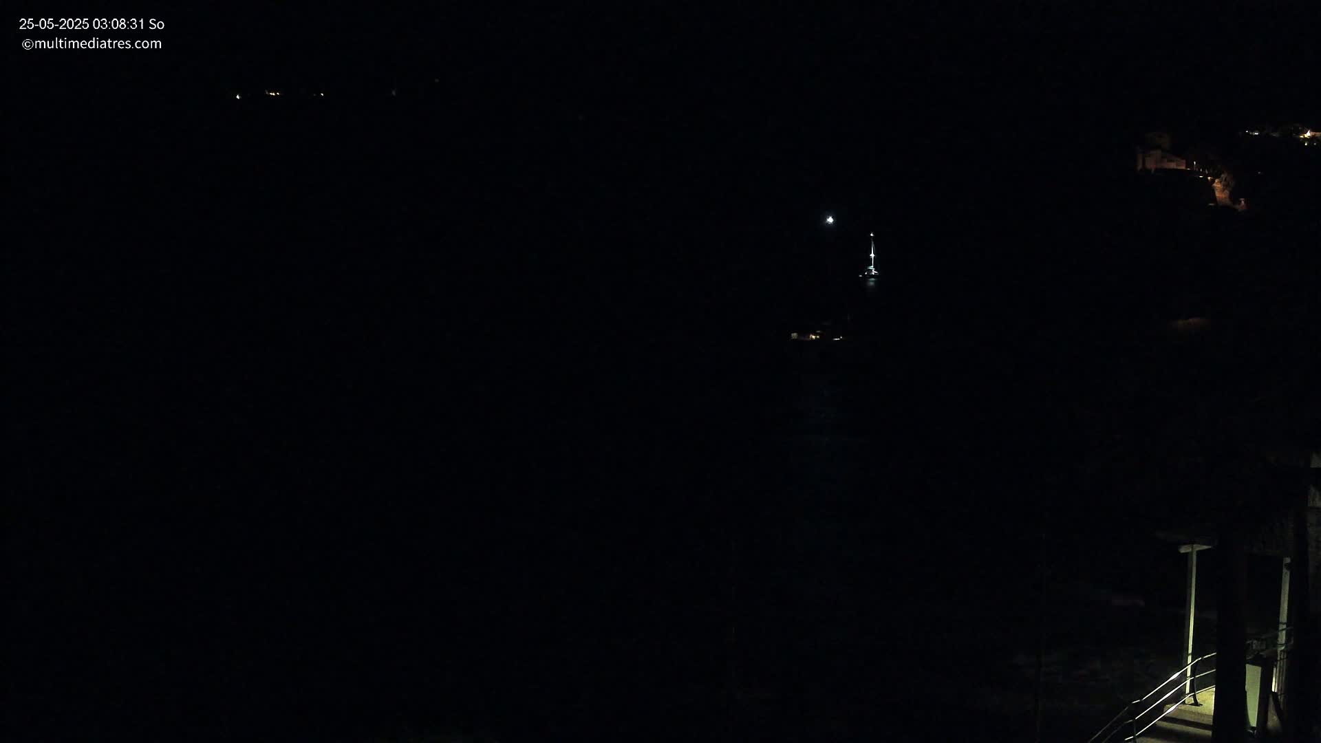 A dark nighttime scene shows a small amount of light from buildings in the distance, along with a small light possibly from a boat on the water.