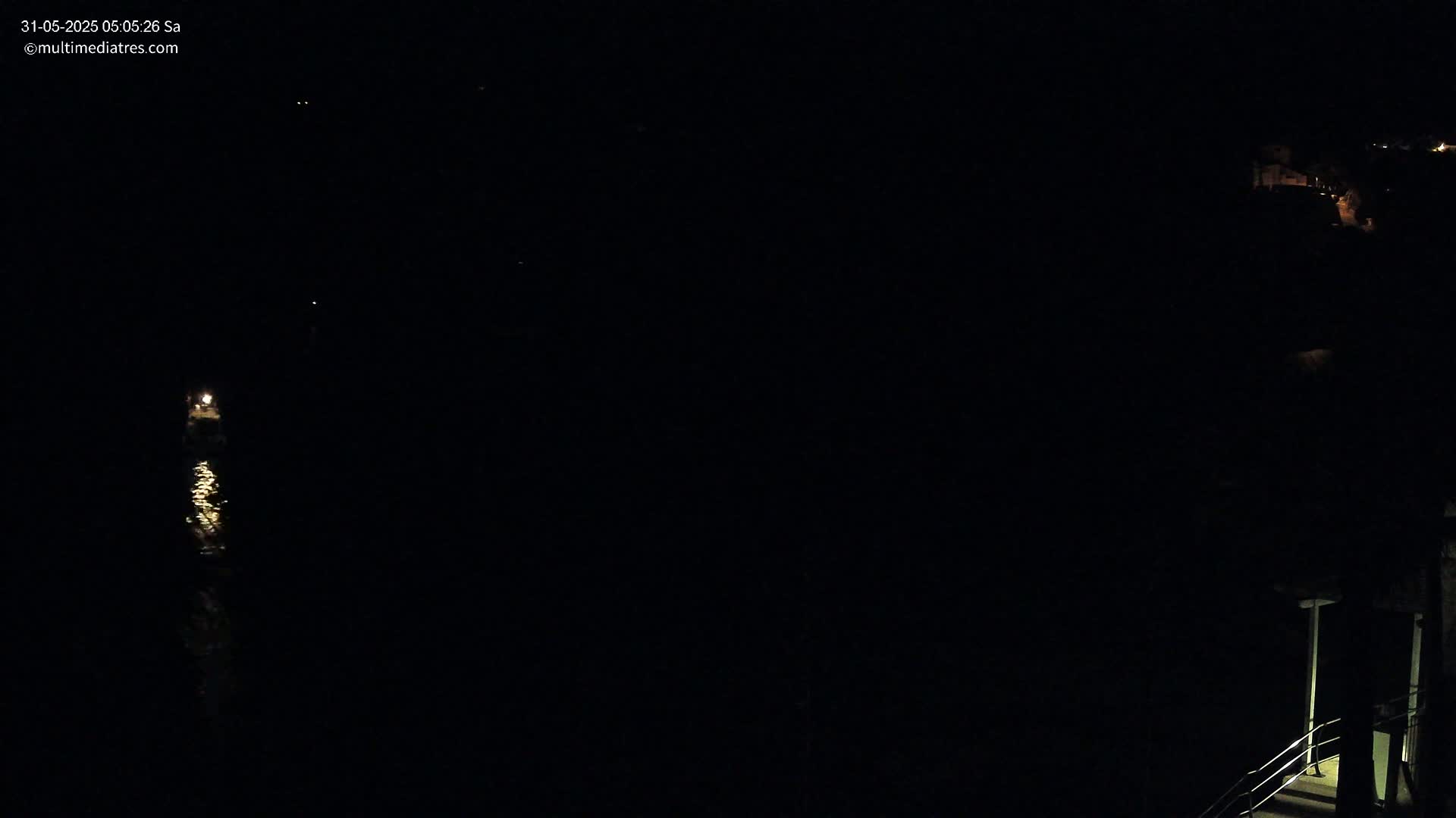 A dark nighttime scene shows a waterway with a single light source reflecting on the water, and a dimly lit structure on the right.