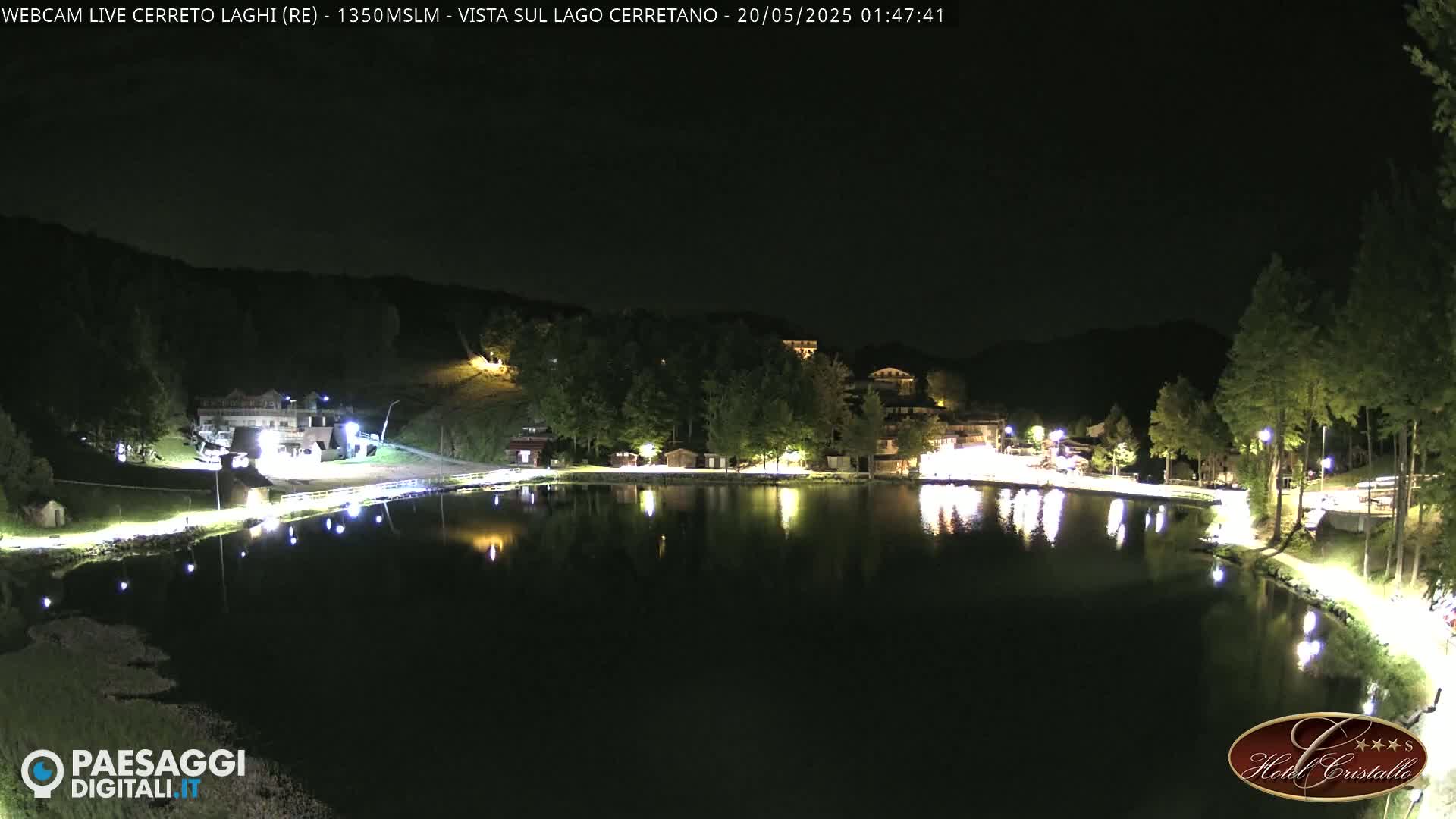 A nighttime view of a calm lake reflecting the lights of buildings and trees on its shores under a clear, dark sky.