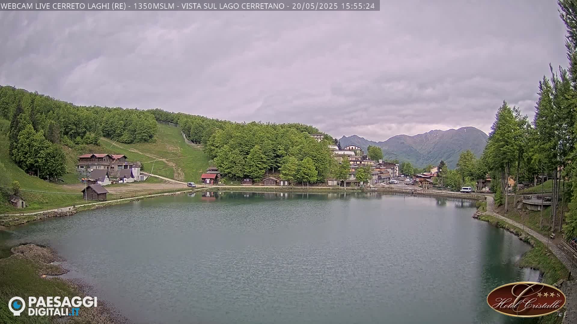 A lake surrounded by a village nestled in a mountainous area under an overcast sky.