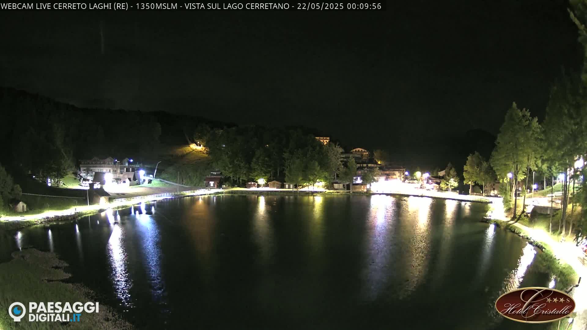 A calm lake at night, reflecting the lights of buildings and trees on its shores under a dark sky.