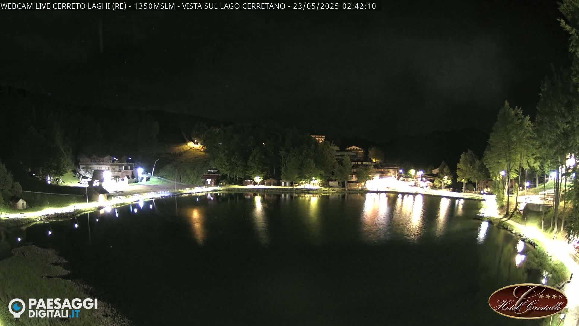 At night, illuminated buildings and trees surround a calm lake reflecting lights.