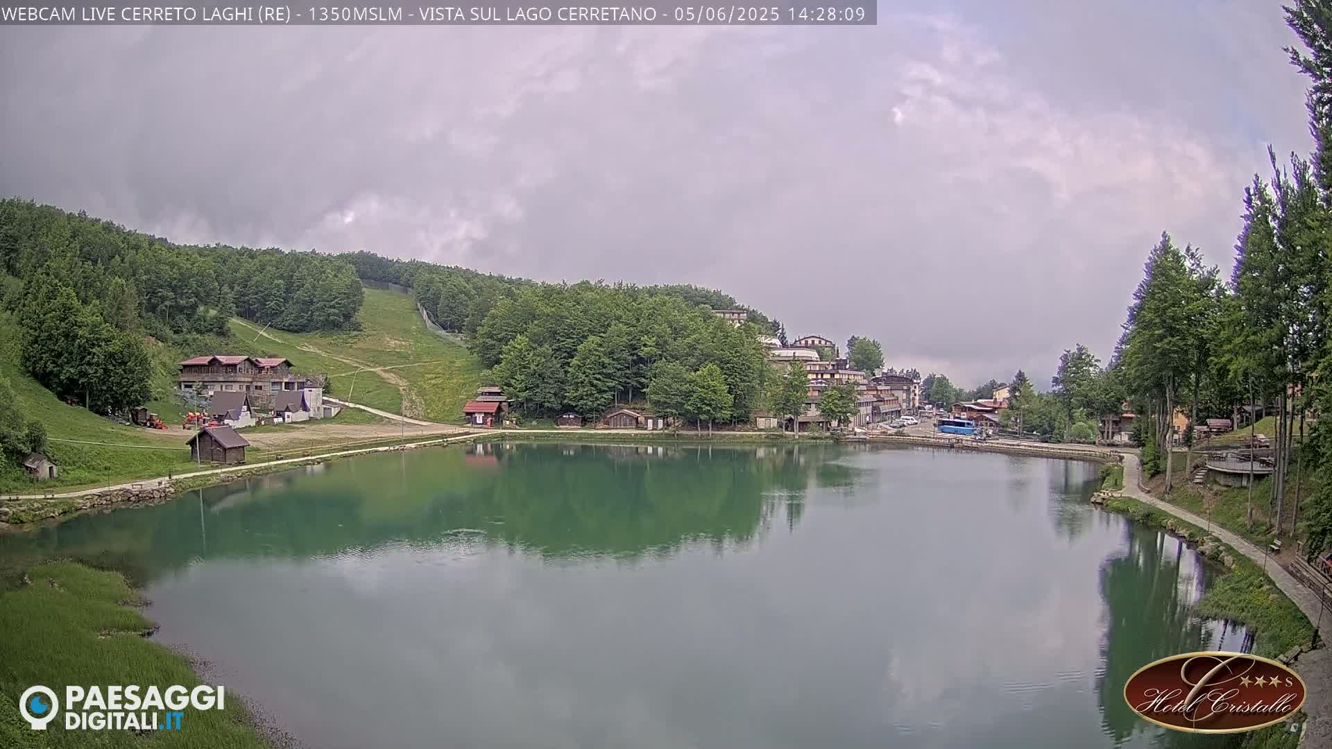A calm lake reflects the overcast sky and surrounding buildings and trees of a mountain resort.