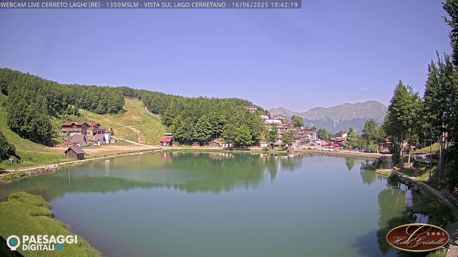 A calm lake reflects buildings and mountains under a clear blue sky.