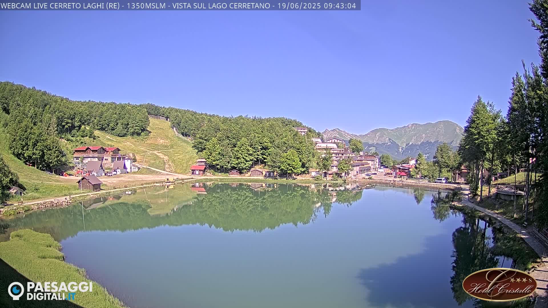 A calm lake reflects buildings and mountains under a clear blue sky.