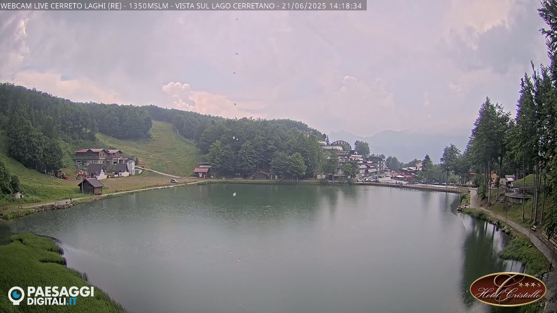 A calm lake sits below a hillside town under a cloudy sky.