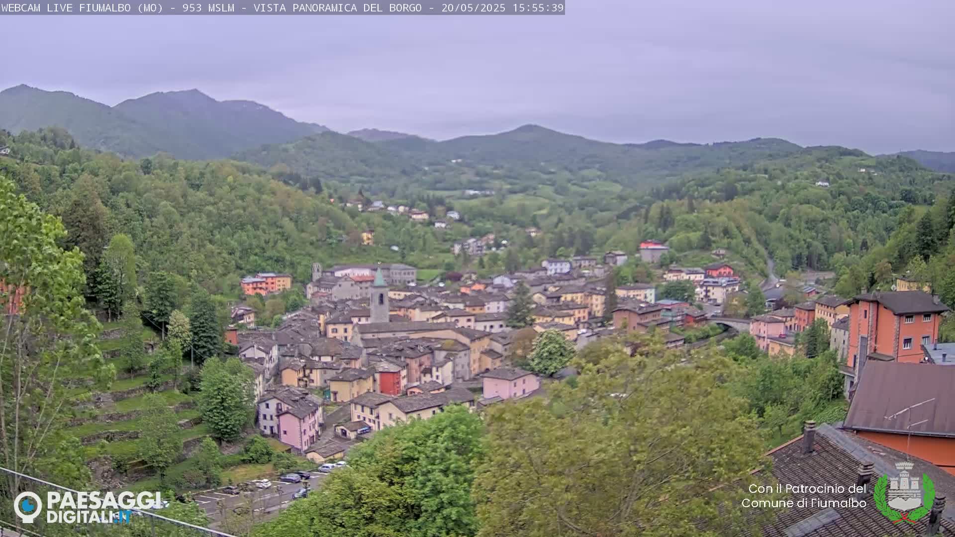 A small town nestled in a valley surrounded by green hills and mountains under an overcast sky.