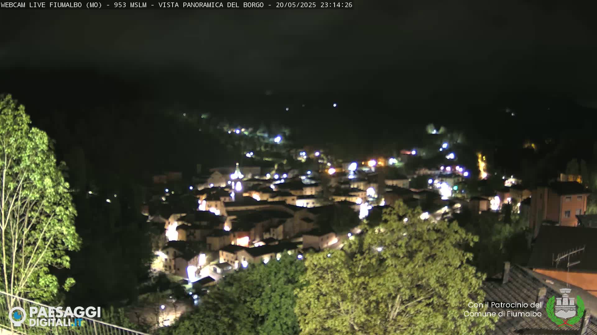 A nighttime, panoramic view of a small town nestled in a valley, illuminated by streetlights and building lights.