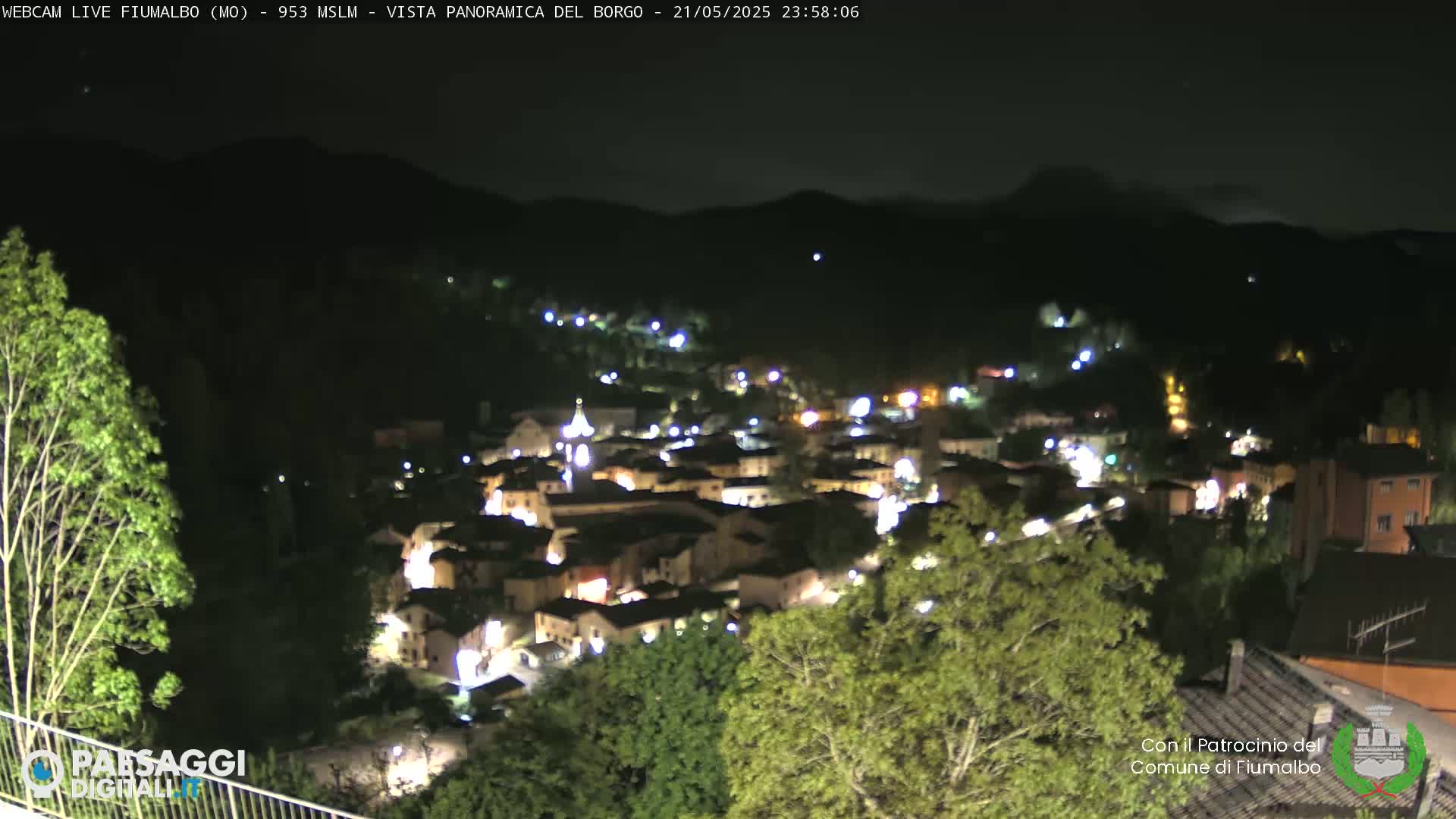 A nighttime, panoramic view of a small, illuminated town nestled in a valley between dark hills.