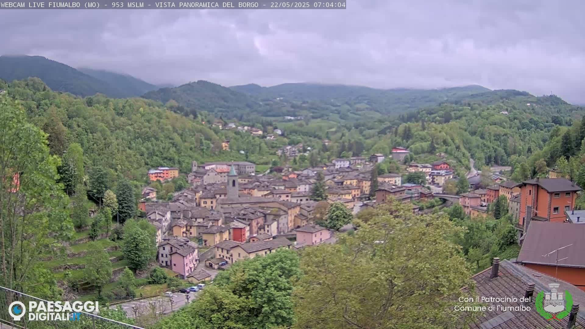 A hillside village nestled in a valley, surrounded by lush green hills under an overcast sky.