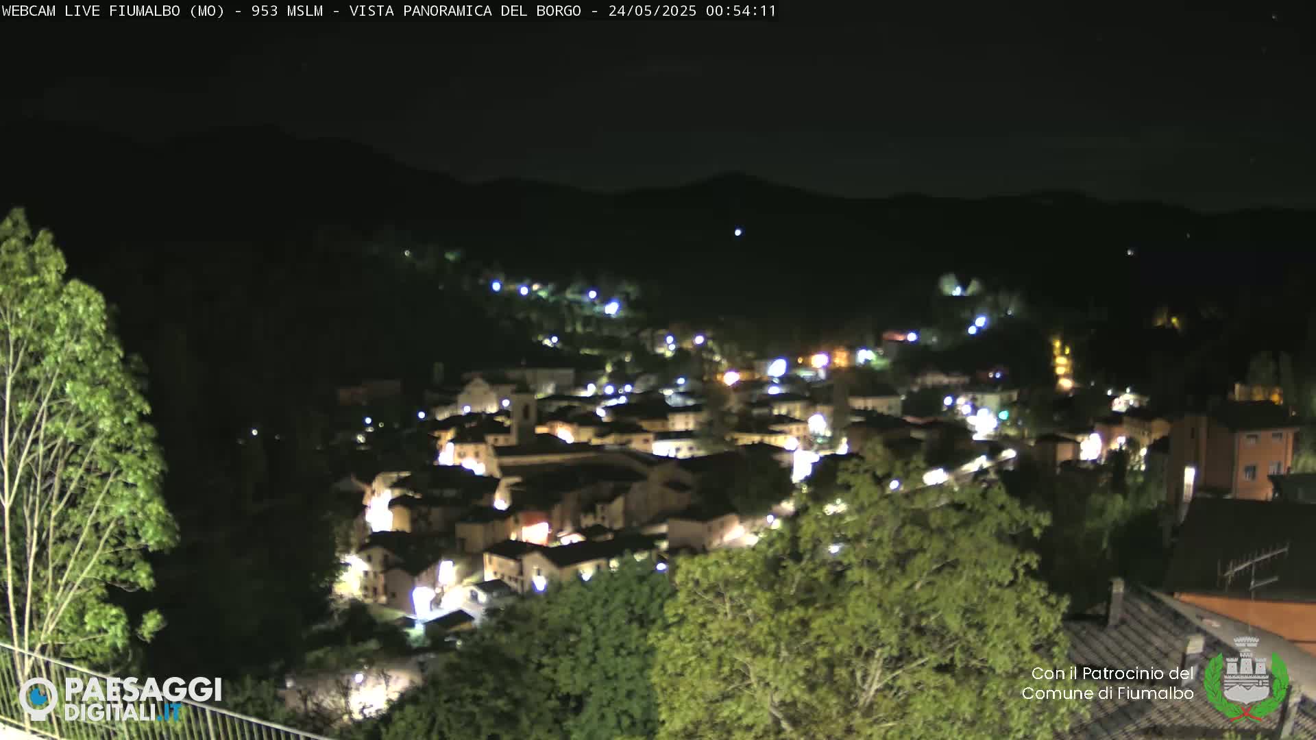 A nighttime, panoramic view of a small town nestled in a valley, illuminated by streetlights.