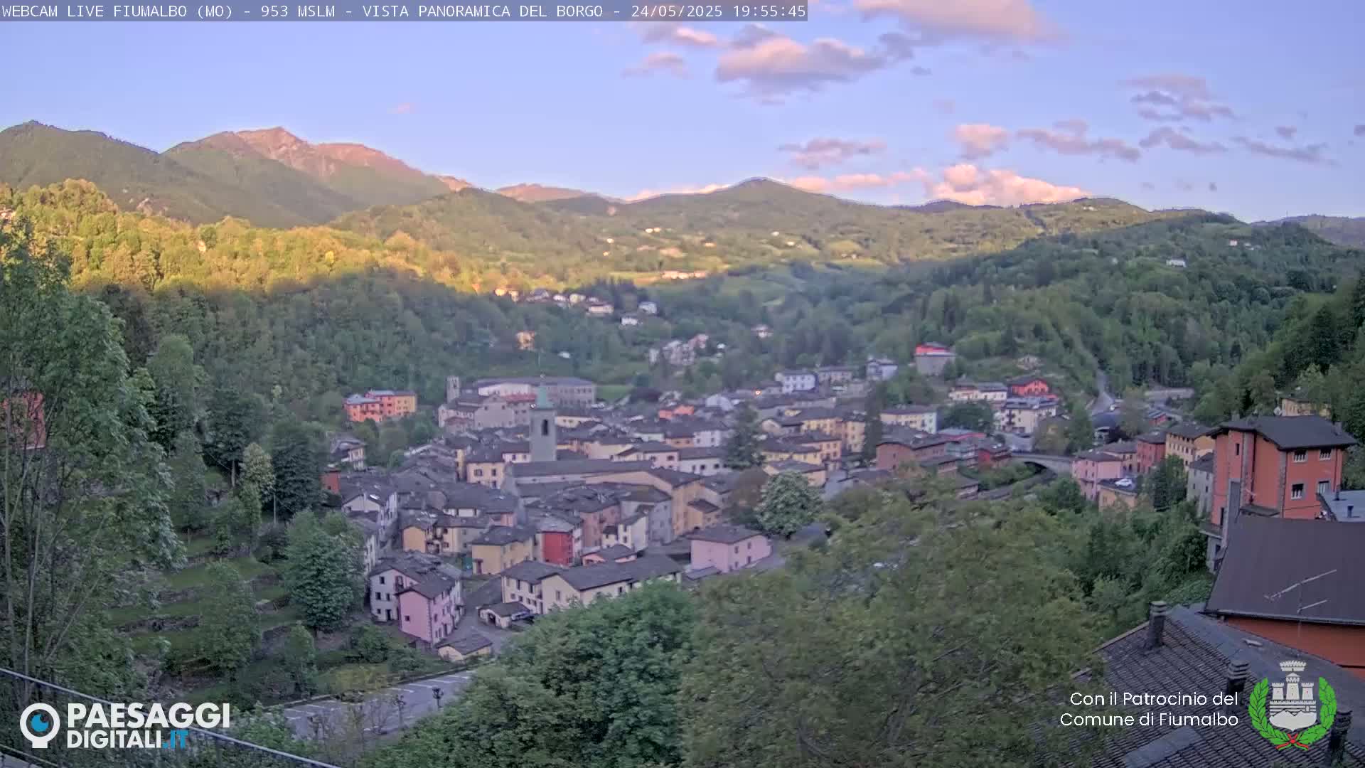 A hillside village nestled in a valley between mountains under a partly cloudy sunset sky.