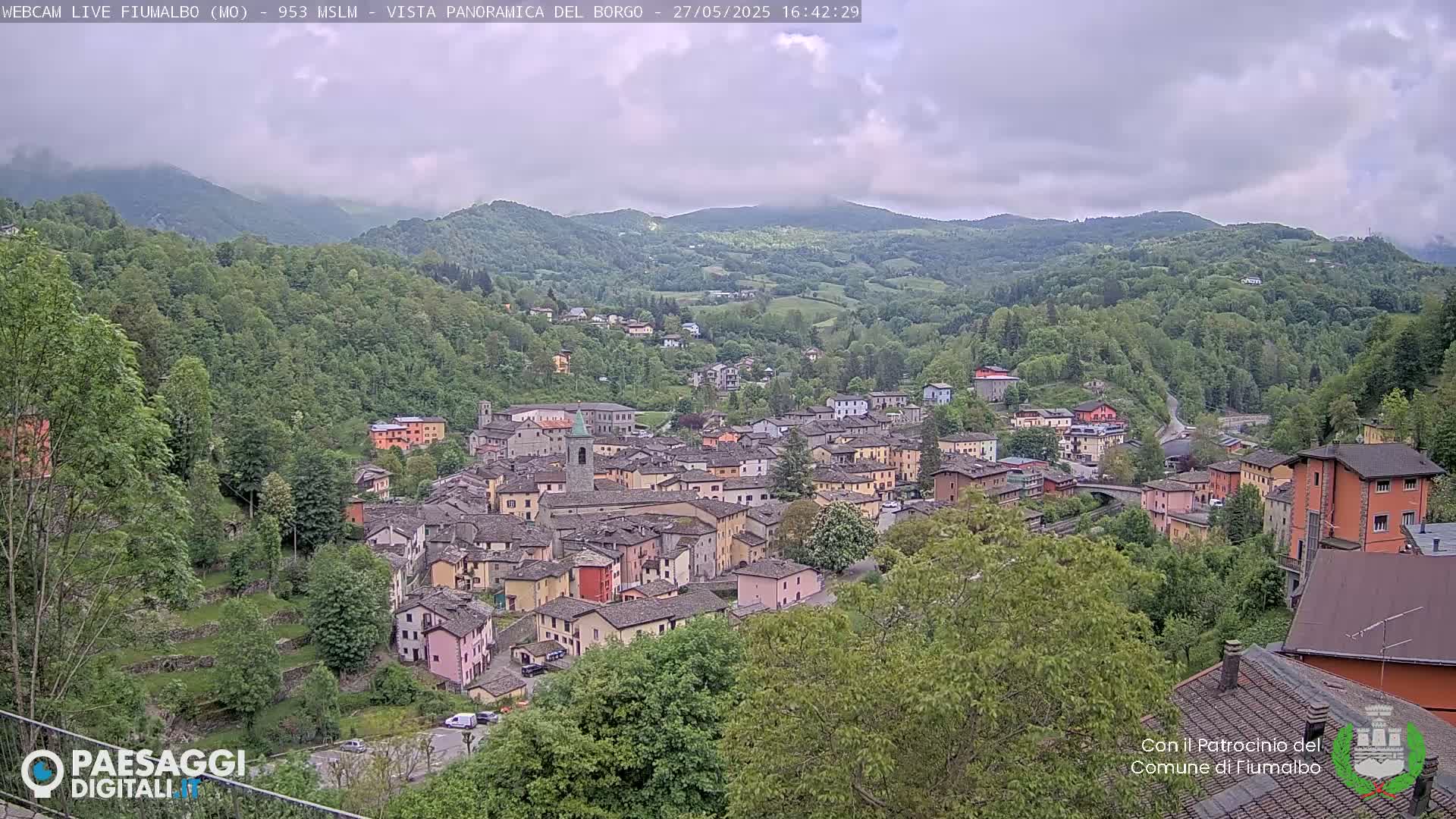 A small town nestled in a valley, surrounded by lush green hills under a partly cloudy sky.