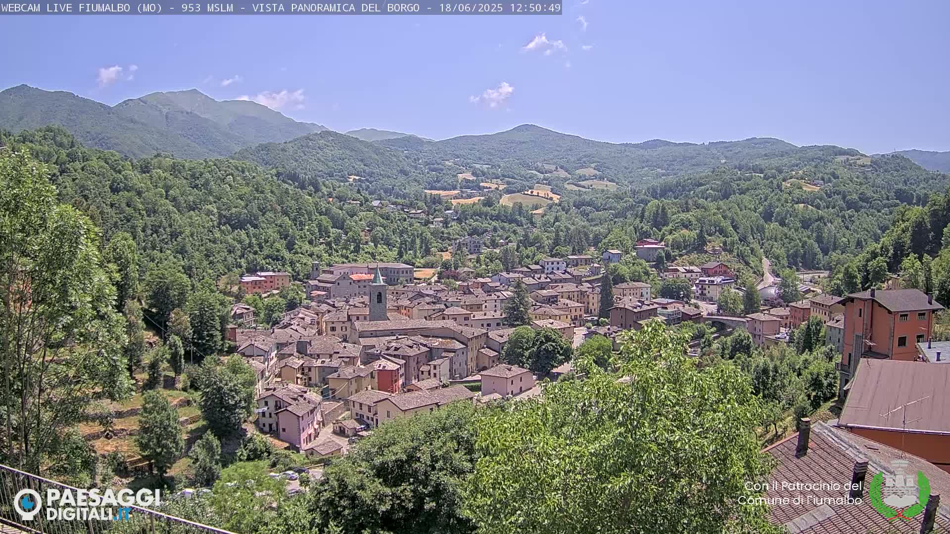 A small town nestled in a valley surrounded by lush green hills and mountains under a clear blue sky.