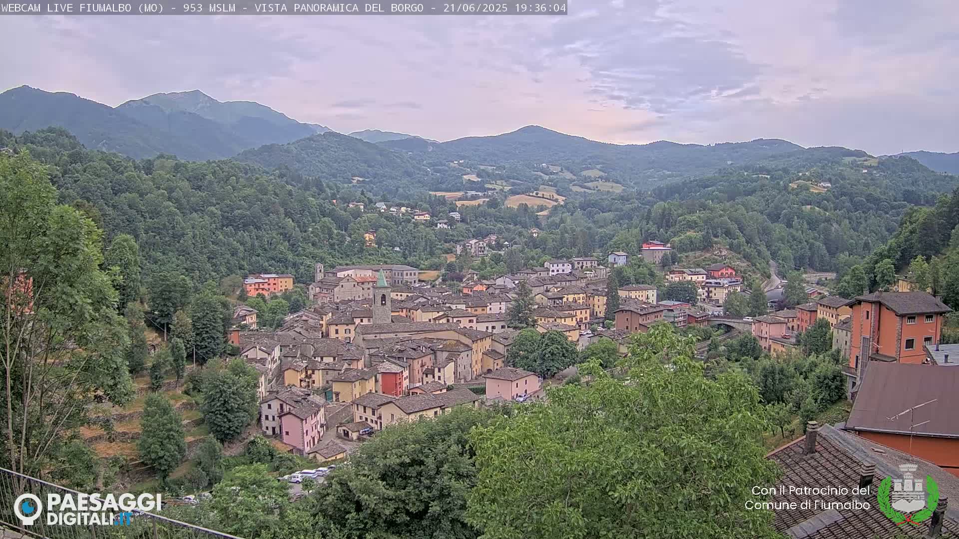 A small town nestled in a valley surrounded by lush green hills and mountains under an overcast sky.